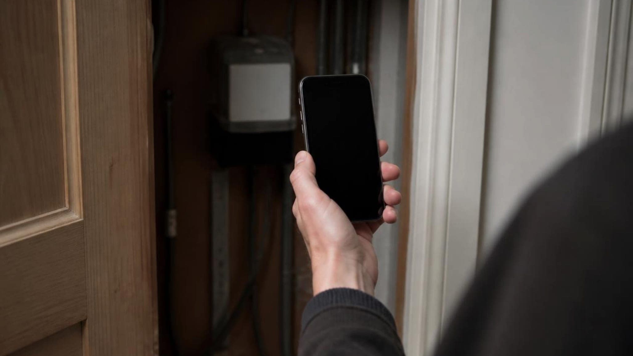 A person holding up a phone to photograph the electricity meter in a cupboard at home